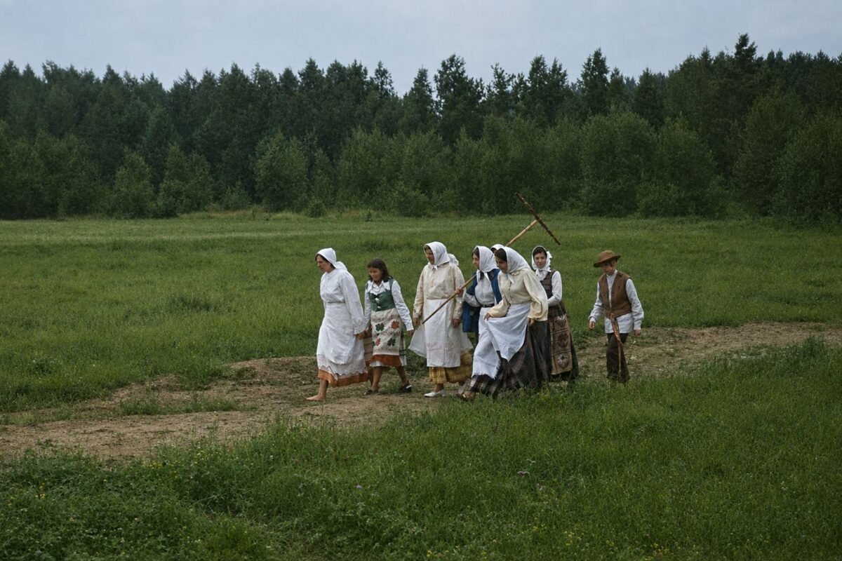 Rugiapjūtės pabaigtuvių dalyviai, apsirengę tradiciniais lietuvių kaimo drabužiais, eina per lauką.