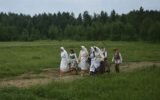Rugiapjūtės pabaigtuvių dalyviai, apsirengę tradiciniais lietuvių kaimo drabužiais, eina per lauką.