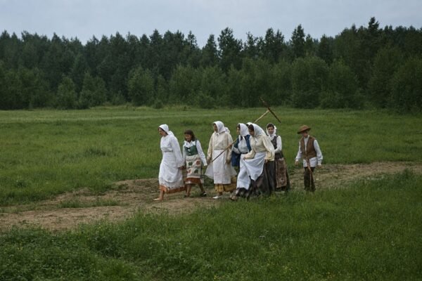 Rugiapjūtės pabaigtuvių dalyviai, apsirengę tradiciniais lietuvių kaimo drabužiais, eina per lauką.