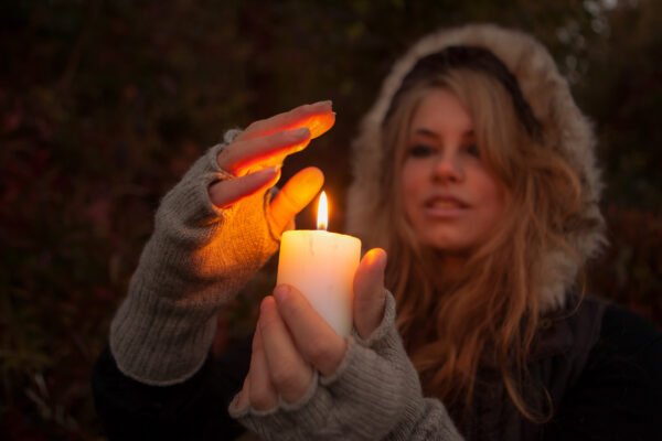 Moteris prieblandoje laiko degančią baltą žvakę ir delnu pridengia jos liepsną.